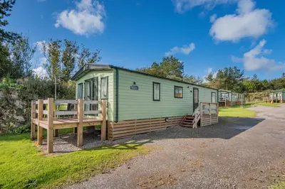 a green tiny house with a porch and a fence at Platinum Holiday Caravan in Bothel