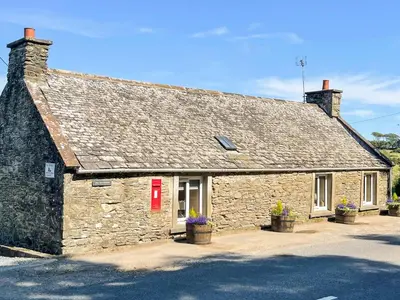 an old stone building with a red door and windows at The Smiddy in Glasserton