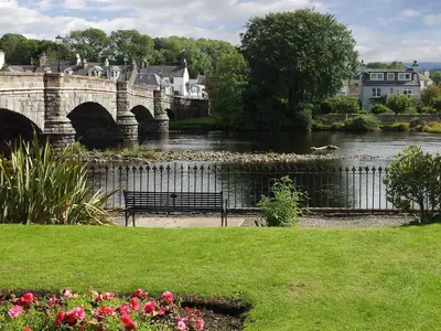 a bench next to a river with a bridge at The Smiddy in Glasserton
