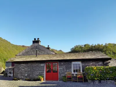 a stone house with a red door and chairs at Field House Bothy - Uk12571 in Borrowdale Valley