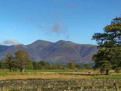 a field with a fence and mountains in the background at Field House Cottage - Uk12573 in Borrowdale Valley