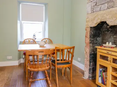 a dining room table with chairs and a fireplace at Daisy Cottage in Moffat