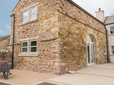 a stone building with a white door and windows at The Barn in Workington