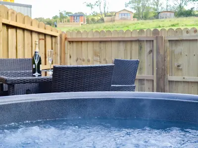 a hot tub in a backyard with chairs and a fence at Curlew in Westward