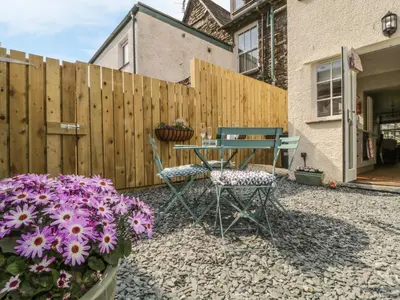 a patio with a table and chairs and flowers at Poppy's Cottage in Ambleside