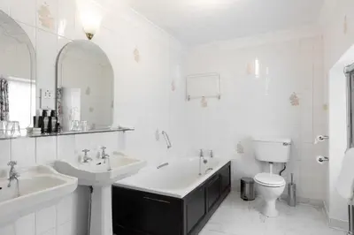 a white bathroom with two sinks and a toilet at Cally Palace Hotel & Golf Course in Gatehouse of Fleet