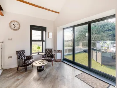 a living room with two chairs and a table and windows at North Plain Barn in Bowness-on-Solway