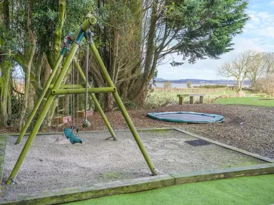 a swing set in a park with a trampoline at North Plain Barn in Bowness-on-Solway