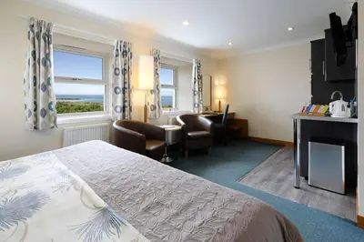 a hotel room with a bed and a desk and chairs at Woodland Bay Hotel in Girvan