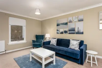 a living room with a blue couch and two chairs at Cairn Suite - Donnini Apartments in Ayr