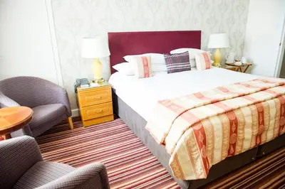 a bedroom with a large bed and two chairs at Eskdale Hotel in Langholm