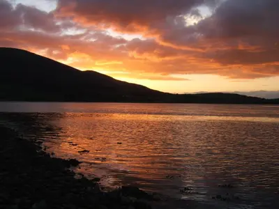 a sunset over a body of water with mountains at Sunset Retreat Lodge with Hot Tub in Carsethorn