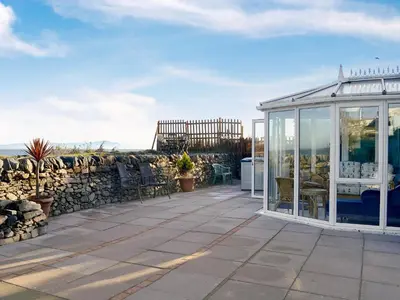 a greenhouse on a patio with a stone wall at Wavecrest in Mainsriddle