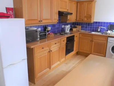 a kitchen with wooden cabinets and blue tiles at Rowan Cottage in New Galloway