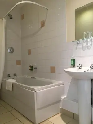 a white bathroom with a tub and a sink at The Sleepwell Inn in Workington
