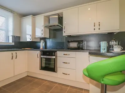 a kitchen with white cabinets and a green chair at Rowan Cottage in St Bees