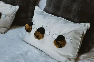a bed with a pillow with embroidered bugs on it at The Huts at Highside Farm in Keswick