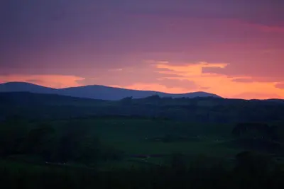 a sunset over a green field with mountains in the background at Craigadam Country House Hotel in Kirkpatrick Durham
