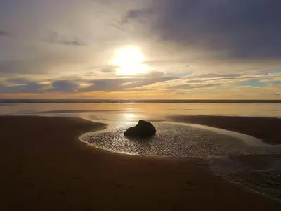 a rock in the sand on a beach with the sunset at THE OLD FARMHOUSE in Holmrook