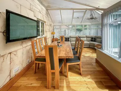 a dining room with a table and a television on a wall at West Fells Cottage in Arlecdon