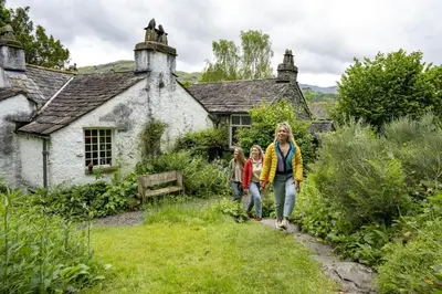 a woman and two children walking in front of an old house at Bakers Retreat spacious 1st floor apartment centrally located in Grasmere in Ambleside