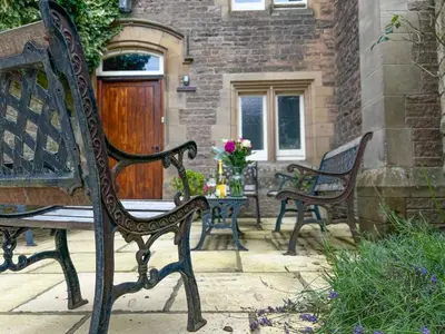 two benches sitting on a patio with a table with flowers at Geltsdale East Wing sleeps 6 with River Eden views near Carlisle & Ullswater in Wetheral
