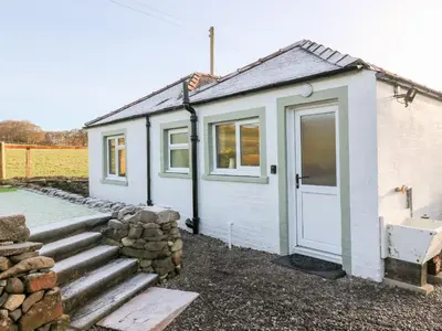 a small white cottage with a door and a stone wall at Glebe Cottage in Dumfries