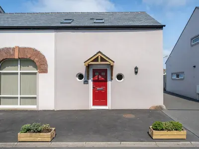 a white house with a red door and two plants at Coney Garth Barn in Beckermet
