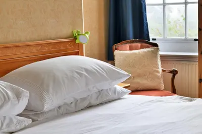 a bed with white pillows and a chair next to a window at Finest Retreats - Edwardian Country House - 9 Bed, Sleeping up to 21 in Longtown