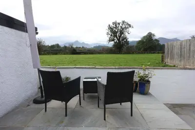 a patio with chairs and a table and a field at Lynton Lodge Studios in Keswick