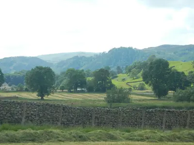 a stone fence with trees and hills in the background at Stybeck Farm in Thirlmere