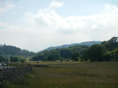 a field with a stone fence and mountains in the background at Stybeck Farm in Thirlmere