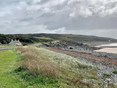a road next to a beach with a house on a hill at Saltlife Cottage in Port William