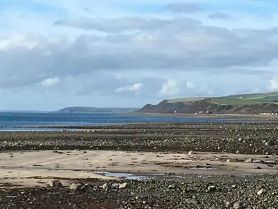 a rocky beach with the ocean and mountains in the background at Saltlife Cottage in Port William