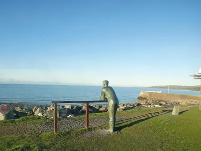 a statue of a man leaning on a rail overlooking the ocean at Killantrae Burn in Port William