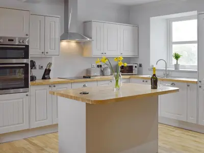 a kitchen with white cabinets and a wooden counter top at The School House in New Luce