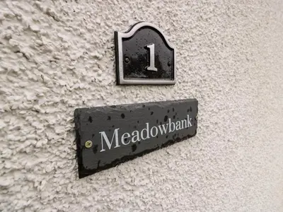 a sign on the side of a wall with a clock at Meadowbank in Girvan