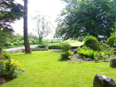 a garden with green grass and trees and bushes at Craignair Cottage in Dalbeattie