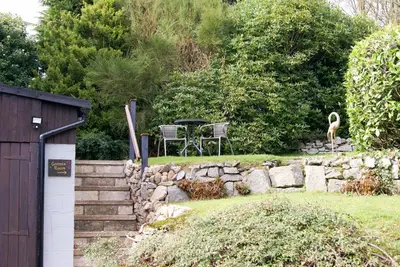 a garden with a stone wall and a table and a bird at Craignair Cottage in Dalbeattie