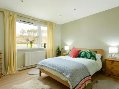 a bedroom with a bed with colorful pillows and a window at Borgan Cottage in Newton Stewart