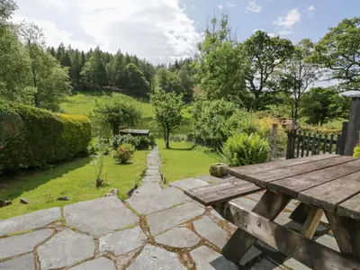 a garden with a wooden picnic table and a stone path at Acorn Cottage in Coniston