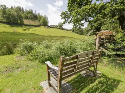a wooden bench sitting in a field of grass at Acorn Cottage in Coniston
