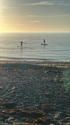 two people are standing on surfboards in the ocean at Reayrt Ny Marrey in Kirkmichael
