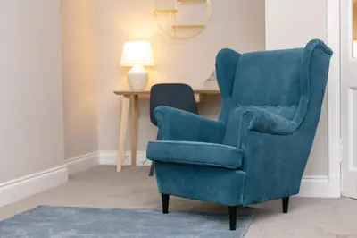 a blue chair sitting next to a desk with a lamp at Seaforth Suite - Donnini Apartments in Ayr