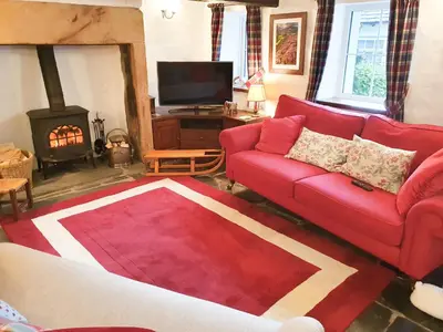 a living room with a red couch and a fireplace at Garden Cottage in Threlkeld