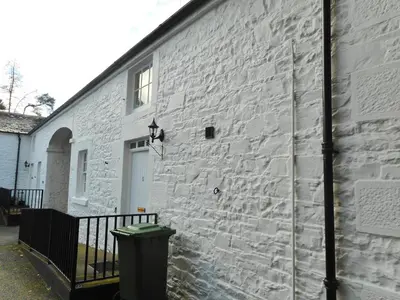 a white brick building with a door and a trash can at DairyCottage, 5, TELFORD MEWS BEATTOCK in Moffat