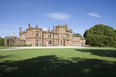 an old castle with a large grass field in front of it at Netherby Hall in Carlisle