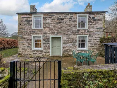 an old stone house with a green door and a table and chairs at Branthwaite Cottage in Caldbeck