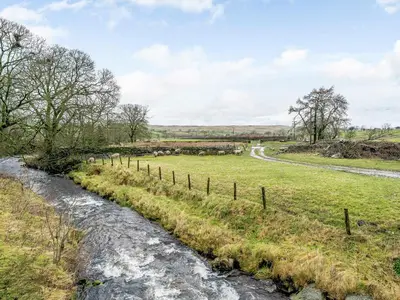 a stream in a field next to a road at Branthwaite Cottage in Caldbeck