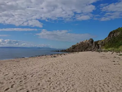a beach with footprints in the sand and the water at Honesty Cottage in Girvan